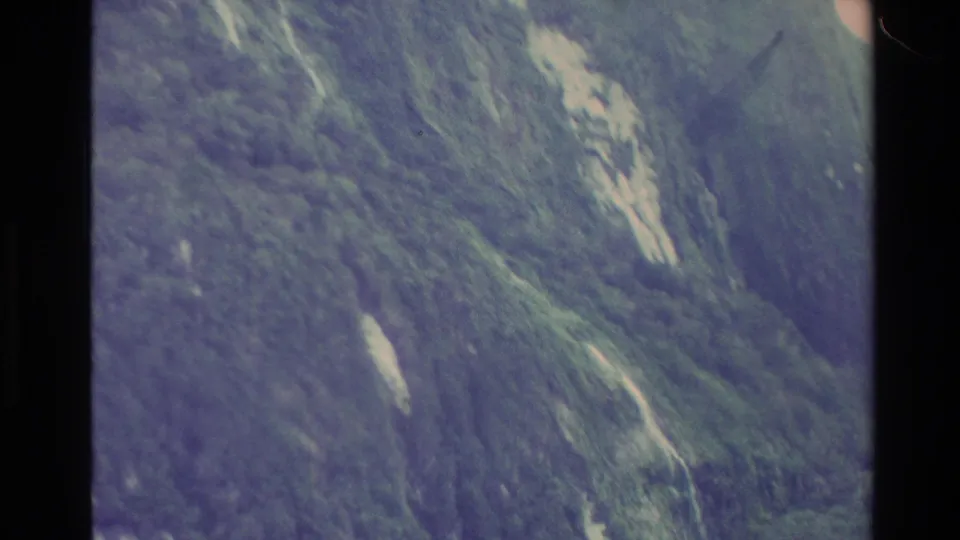 New Zealand 1982 8mm view of a rugged green mountainside with pale cliff streaks and heavy edge shadow.