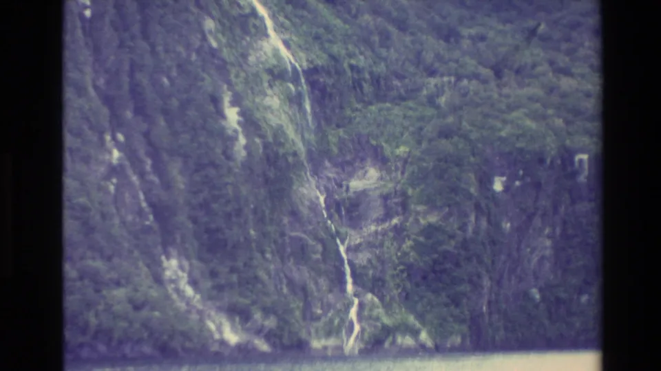 New Zealand 1982 8mm frame showing a narrow waterfall running down a green cliff to the lake below.