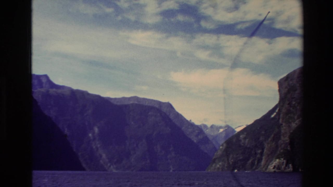 Dark mountain slopes frame a blue fjord under a partly cloudy sky.