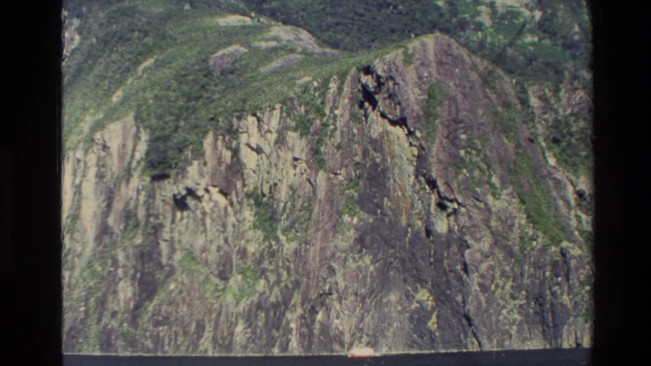 Steep green and gray cliff face seen from above, with film borders around the frame.