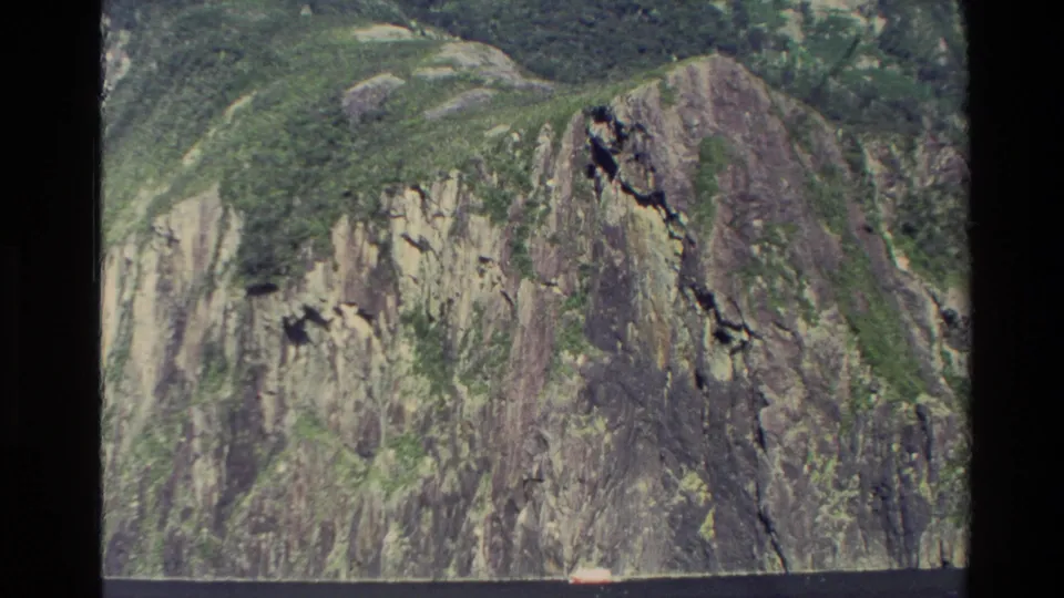 1982 New Zealand 8mm aerial view of a rugged cliff face with green vegetation and exposed rock.