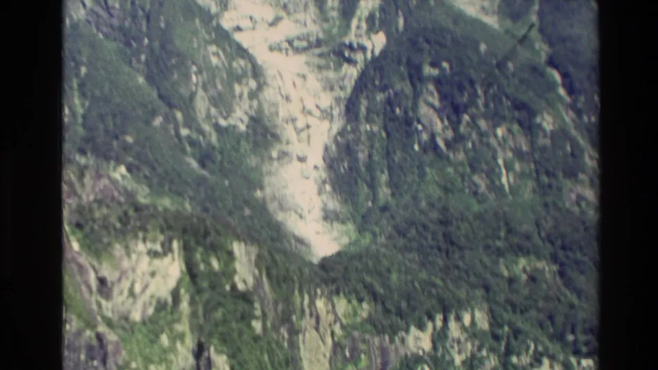 1982 New Zealand 8mm aerial view of a pale rock gully or chute between forested mountain slopes.