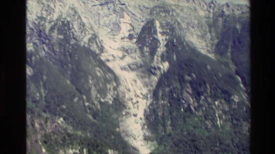 1982 New Zealand aerial frame of rugged slopes with pale rock channels, green vegetation, and soft 8mm texture.