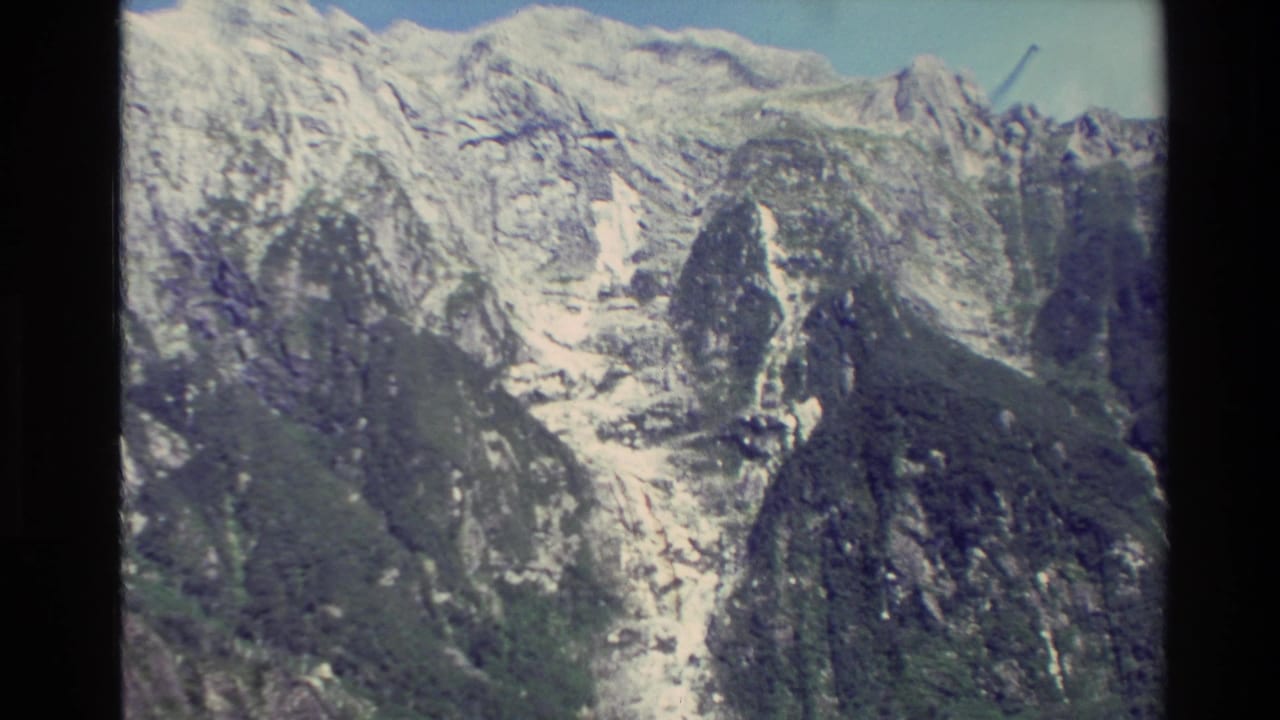 1982 New Zealand 8mm frame showing rugged snow-dusted mountain peaks and rocky slopes beneath a pale blue sky.