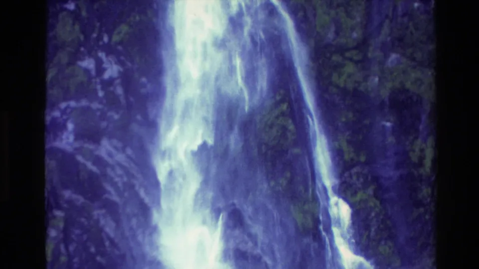 1982 New Zealand 8mm frame with bright cascading water cutting down a shaded, forested rock face.