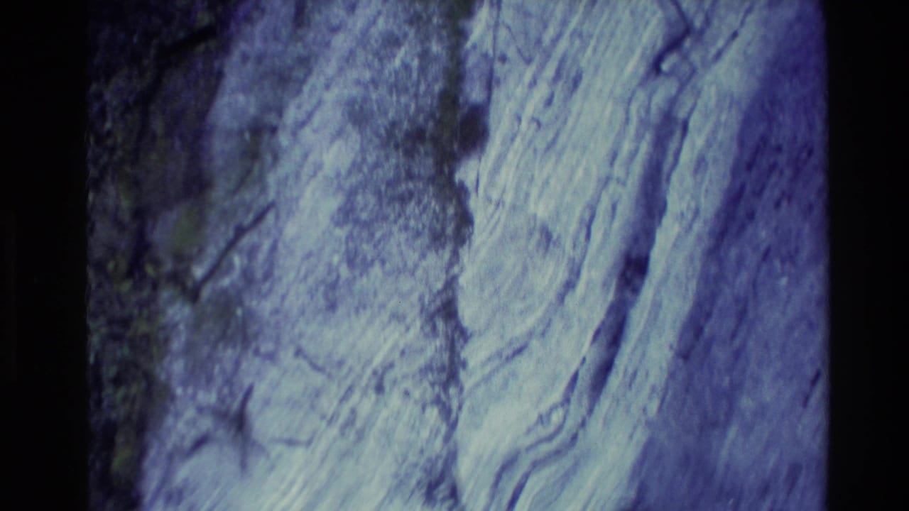 1982 New Zealand 8mm frame showing a close, abstract view of layered rock surfaces with cool color shift and shadowed edges.