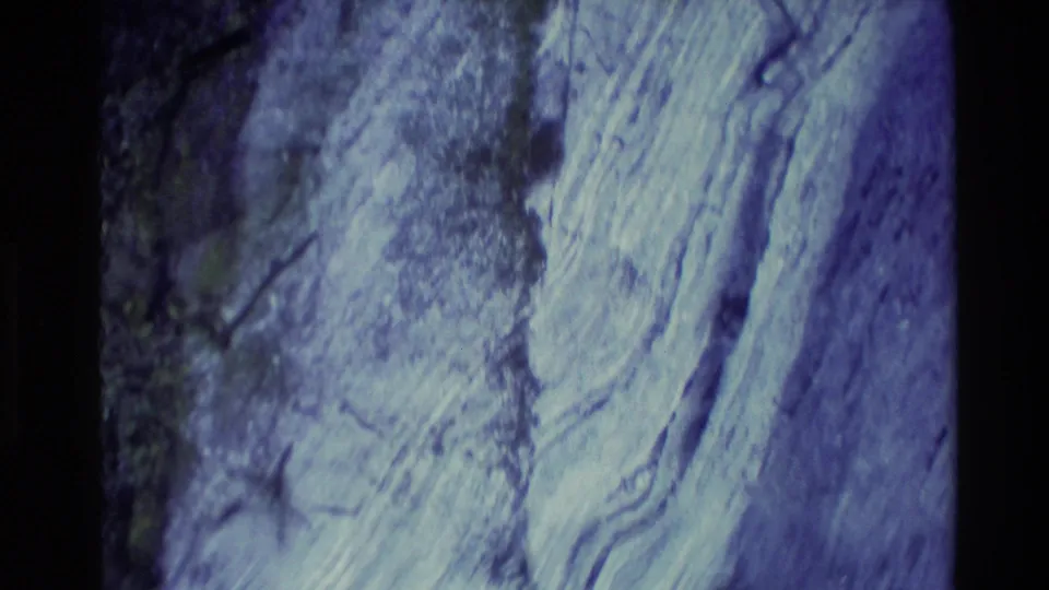 1982 New Zealand 8mm frame showing a close, abstract view of layered rock surfaces with cool color shift and shadowed edges.