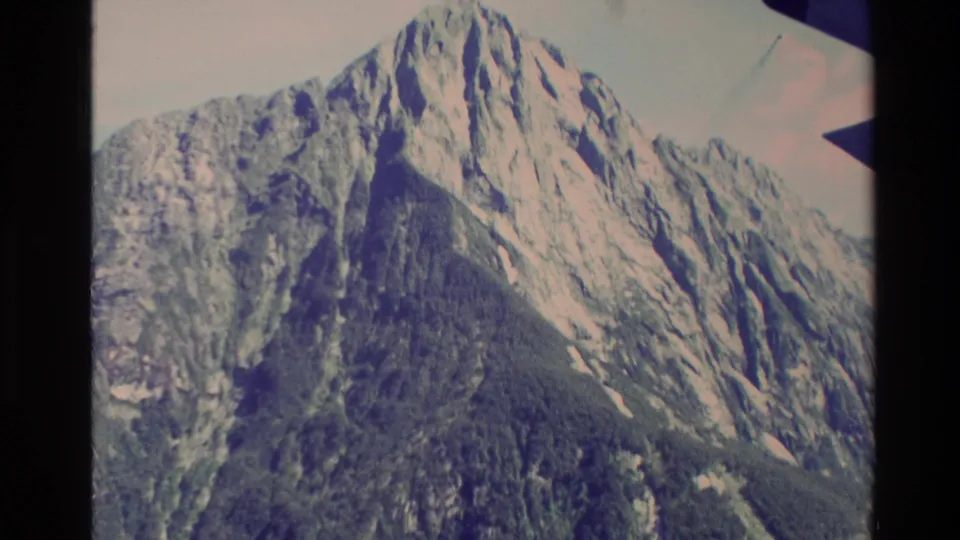 1982 New Zealand 8mm frame showing a tall mountain peak with pale rock or snow patches above dark forested lower slopes.