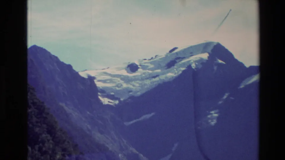 1982 New Zealand 8mm frame centered on a snow-covered mountain shoulder with dark rock, sky, and visible film marks.