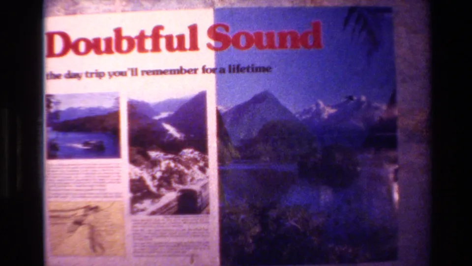 1982 New Zealand home-movie frame showing a Doubtful Sound promotional poster with mountain and lake photographs.