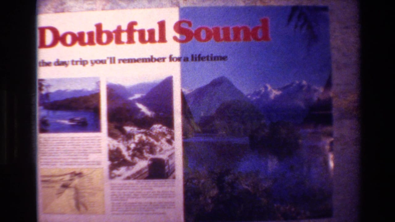 1982 New Zealand home-movie frame showing a Doubtful Sound travel sign with mountain and fjord imagery.