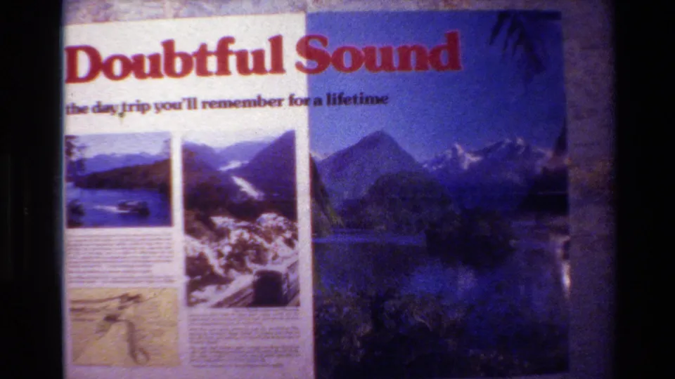 Home-movie frame from New Zealand showing the Doubtful Sound travel headline and printed scenic panels.
