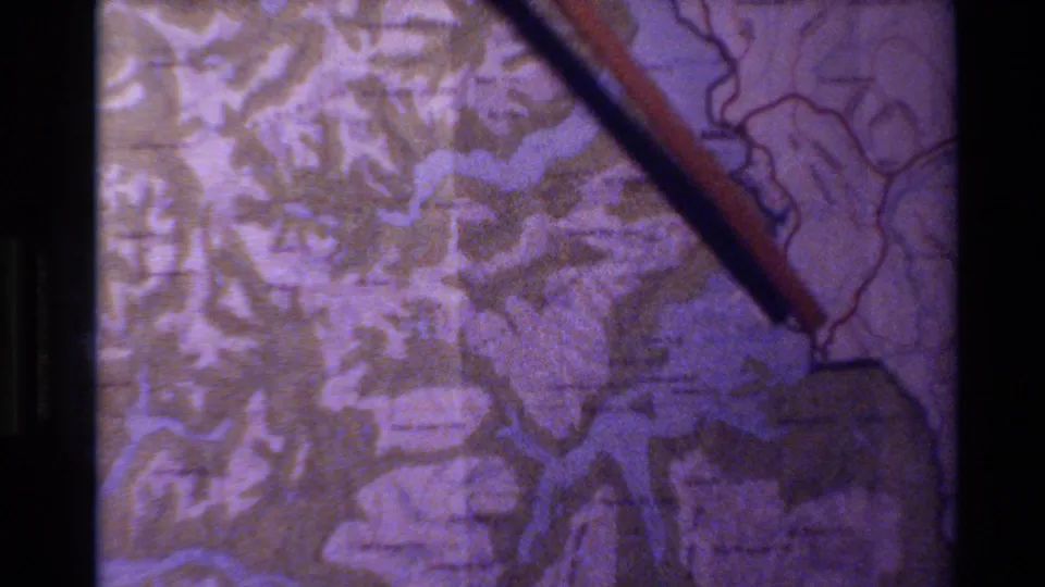 1982 New Zealand home-movie frame showing a hand-held pointer near a projected map or travel display.