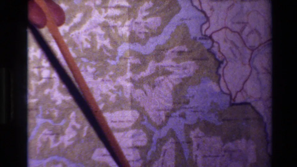 1982 New Zealand home-movie frame showing a stick pointing at a printed topographic map with waterways and terrain markings.