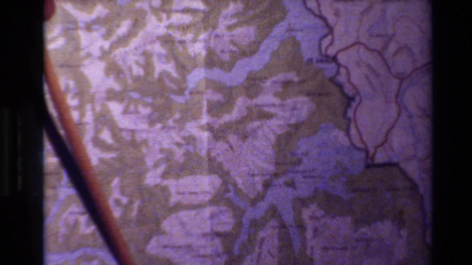 A pointer stick crosses a printed map in this 1982 New Zealand travel clip, with waterways and relief detail visible.