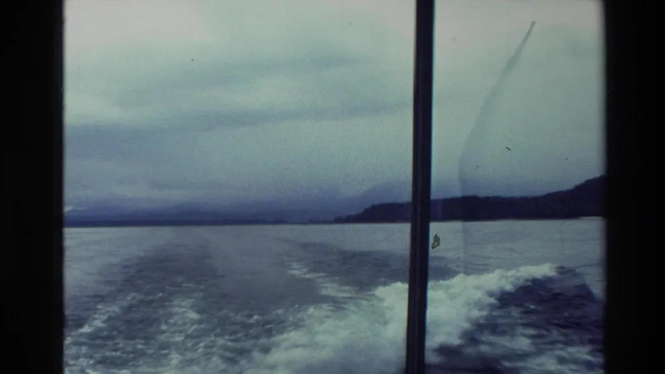 1982 New Zealand 8mm travel footage showing a boat wake through window framing, with open water, low shore, and overcast sky.
