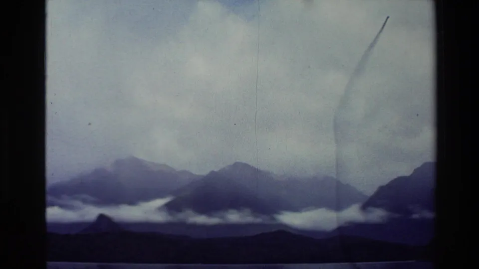 1982 New Zealand 8mm footage looking from a boat window toward dark mountain ridges partly covered by low cloud.