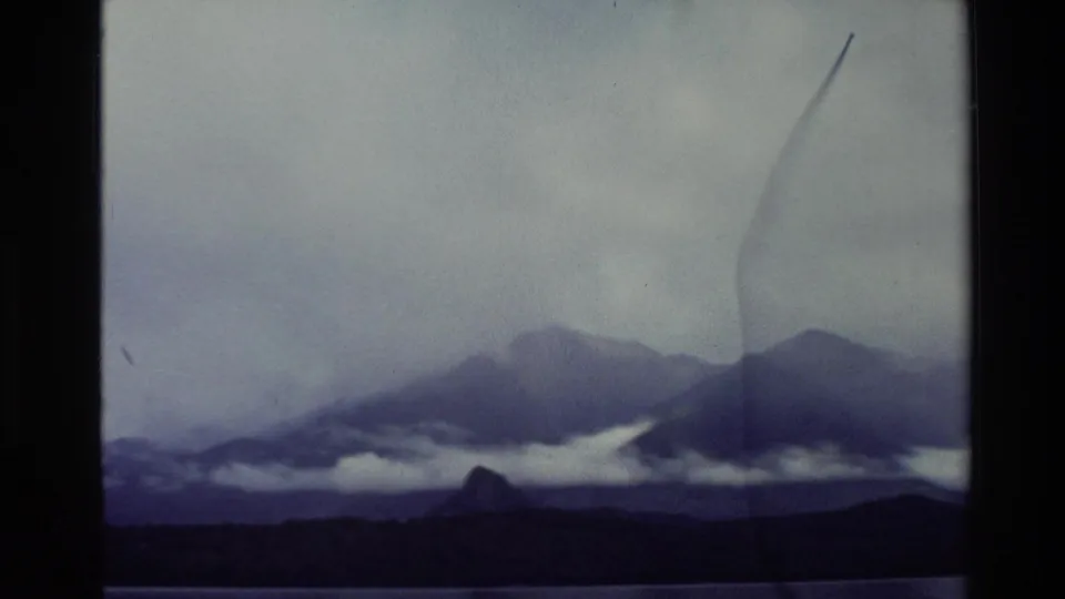 1982 New Zealand home-movie frame showing clouded mountain ridges and a dark shoreline through the boat window.