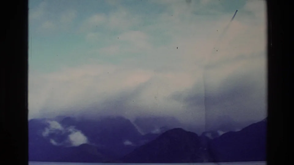 1982 New Zealand 8mm frame with cloud banks drifting across dark mountain ridges above a narrow band of lake.