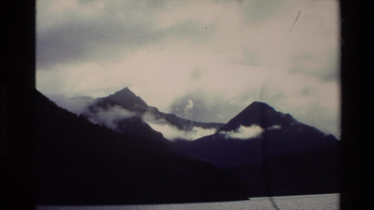 Dark mountain peaks across water with low white mist and cloudy sky.
