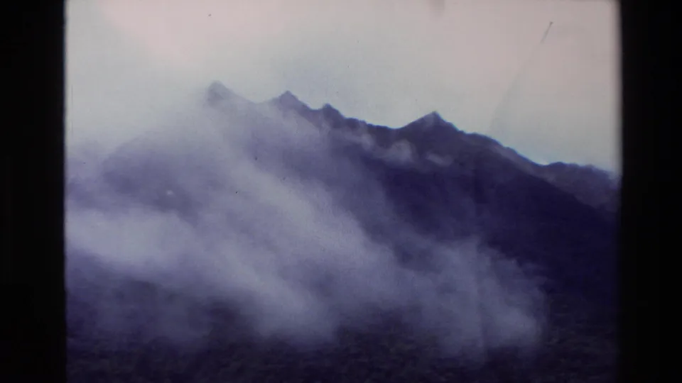 1982 New Zealand 8mm frame with mist covering rugged mountain tops beside a lake under pale cloud.
