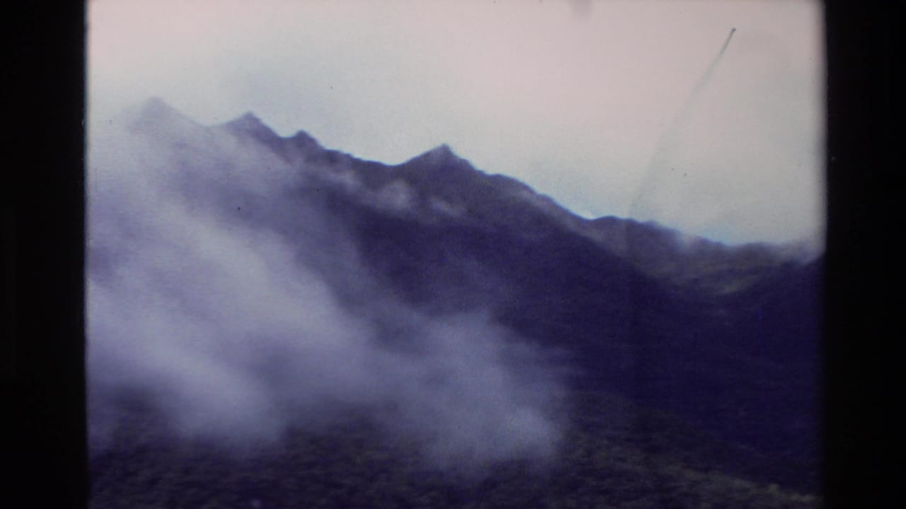 1982 New Zealand Super 8 frame showing mist and clouds around rugged mountain ridges under an overcast sky.