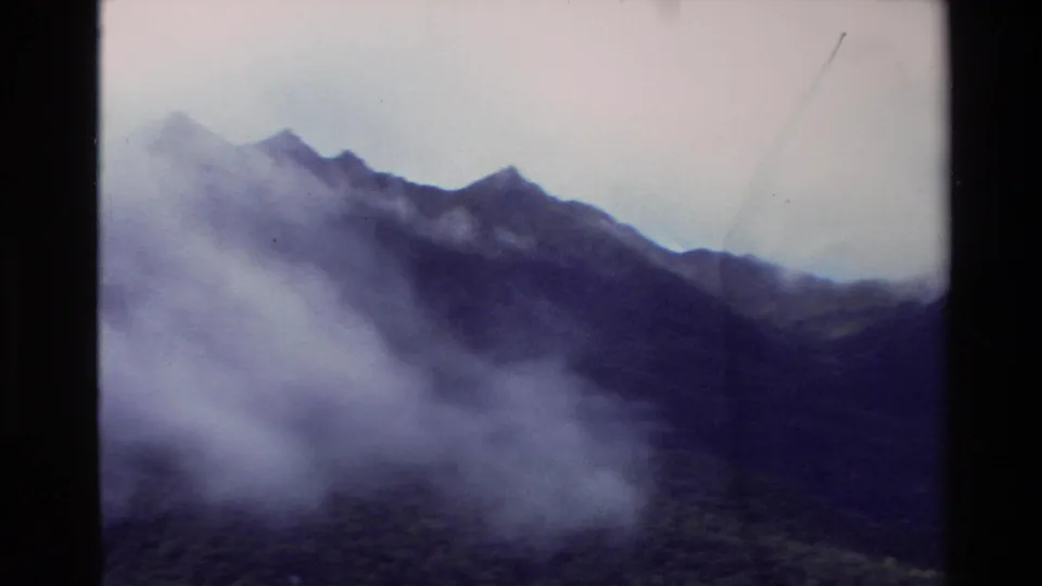 1982 New Zealand Super 8 frame showing mist and clouds around rugged mountain ridges under an overcast sky.