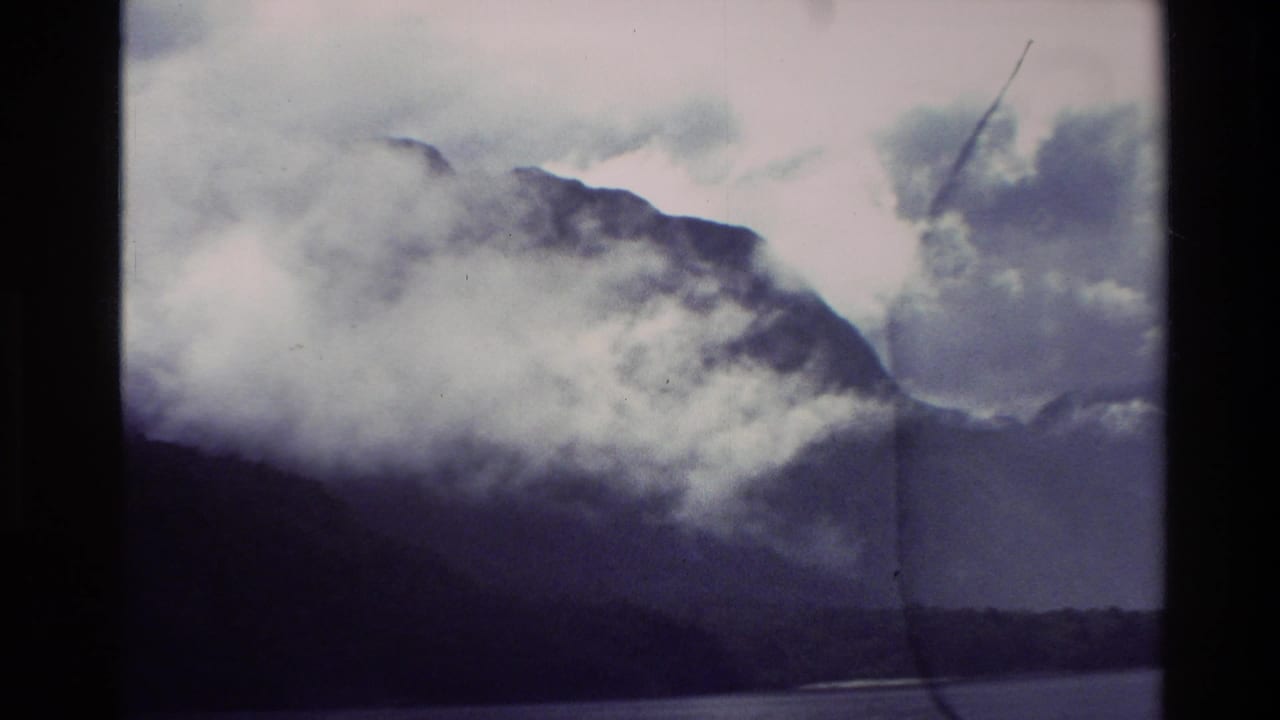 Misty mountain ridge above dark water with clouds hanging low across the peaks.