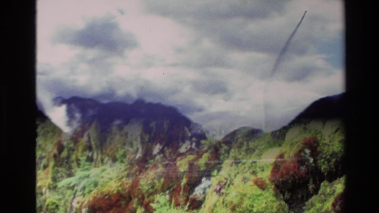 1982 New Zealand 8mm frame showing low cloud over rugged mountain ridges and a green foreground hillside.