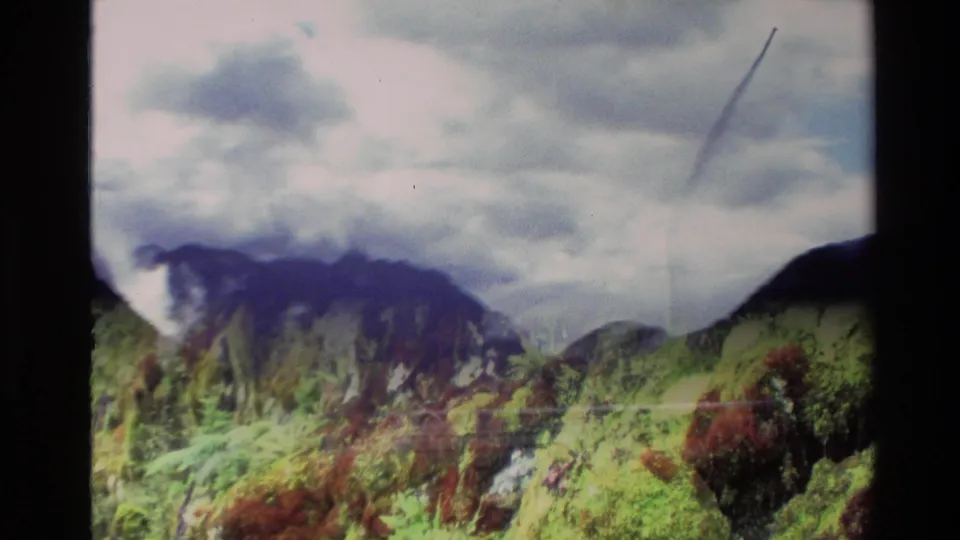 1982 New Zealand 8mm frame showing low cloud over rugged mountain ridges and a green foreground hillside.