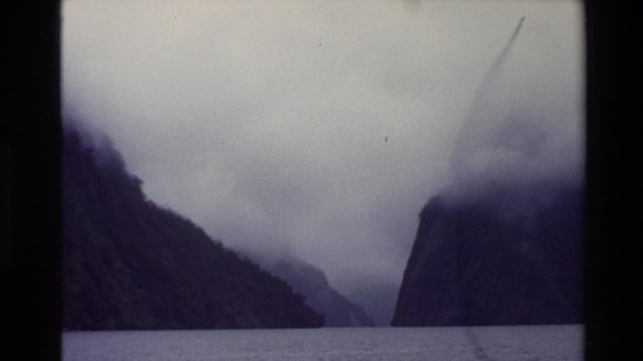 Misty fjord or mountain lake bordered by steep dark cliffs under low cloud.