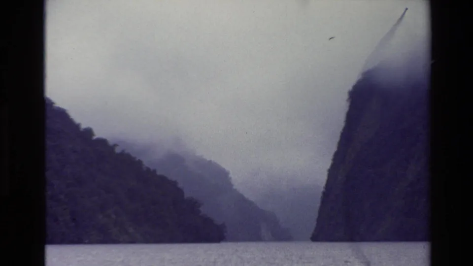 1982 New Zealand 8mm frame showing a misty mountain waterway with dark cliffs receding into cloud.