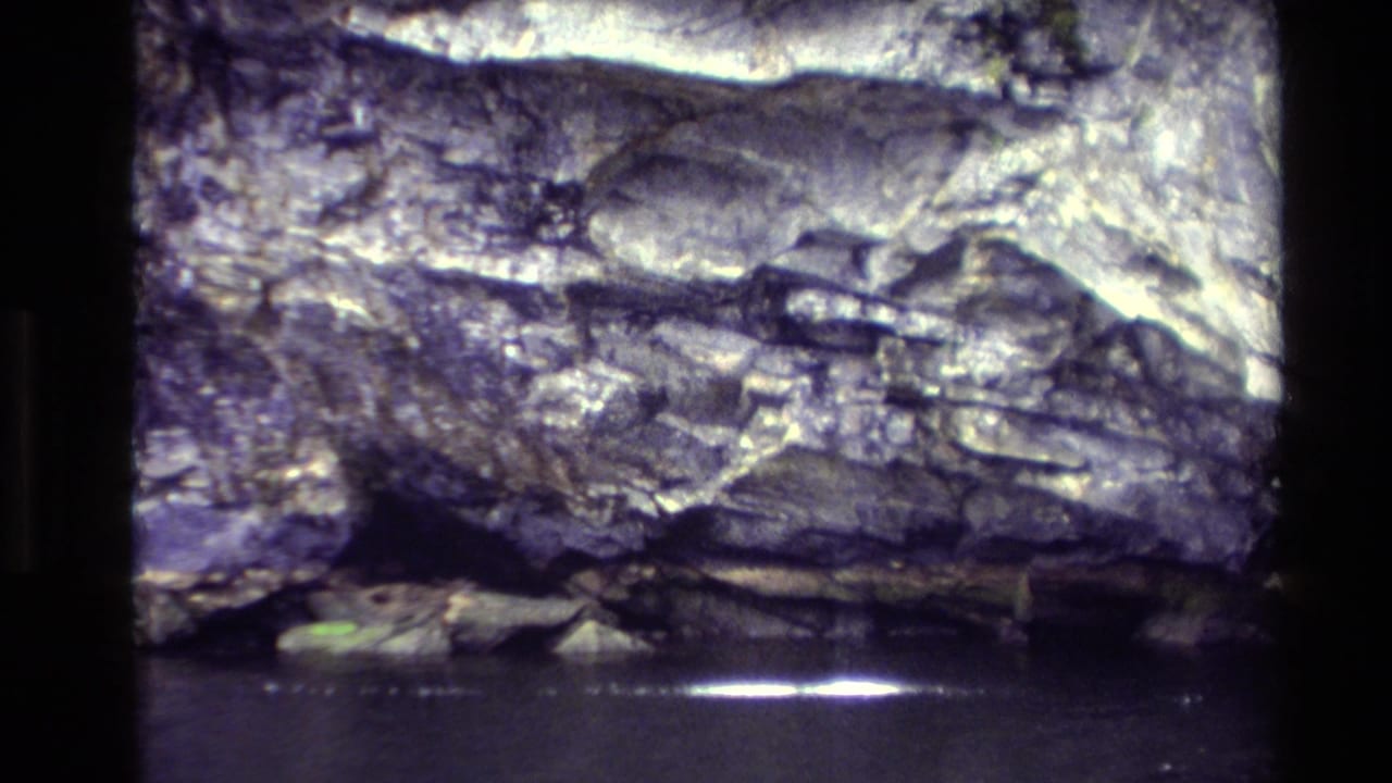 1982 New Zealand 8mm frame showing a rugged rock face above dark water, with soft grain and heavy gate borders.