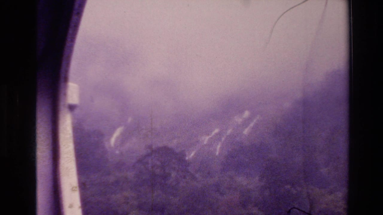 1982 New Zealand 8mm frame showing a smoke-filled mountain view through dark window-like borders, with pale plume streaks on the slope.