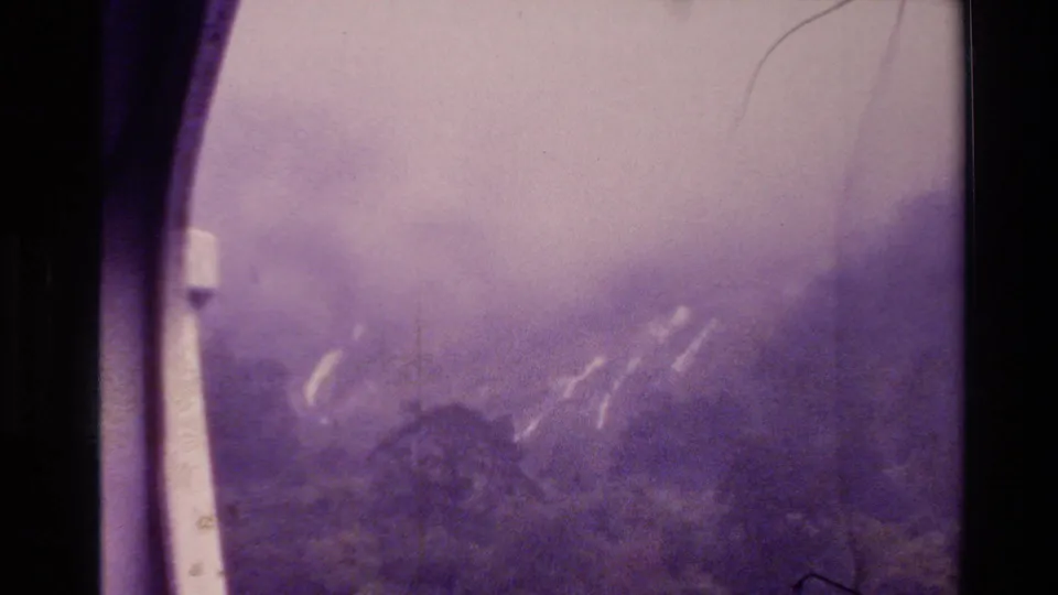 1982 New Zealand 8mm frame showing a smoke-filled mountain view through dark window-like borders, with pale plume streaks on the slope.