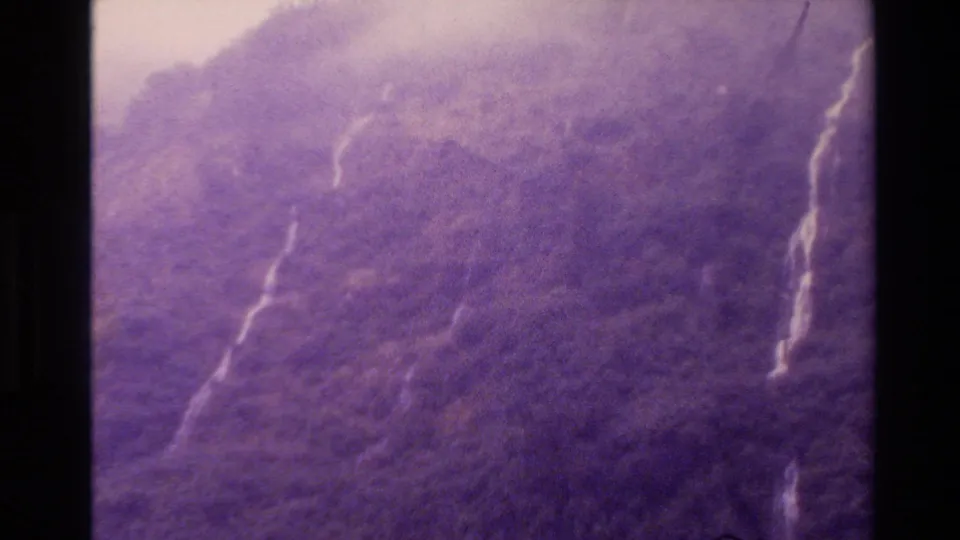 1982 New Zealand 8mm frame showing a hazy wooded hillside, with soft focus, purple fading, and pale vertical streaks on the terrain.