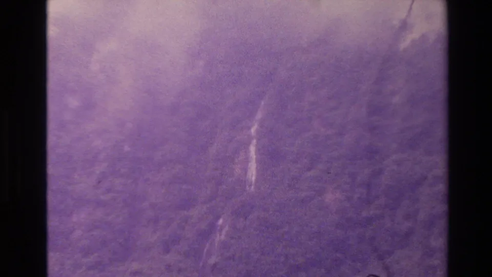 1982 New Zealand 8mm frame with a thin white waterfall cutting through a hazy forested mountainside.
