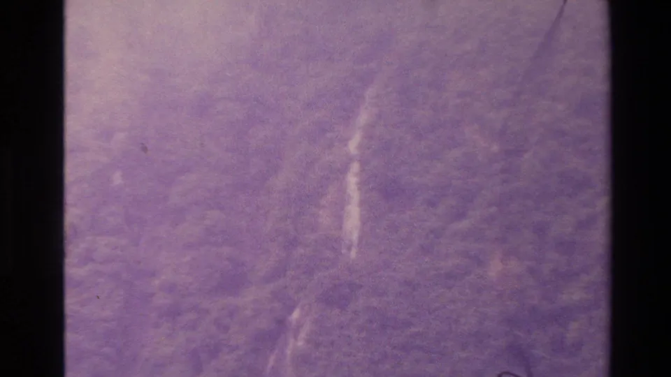Purple-shifted 1982 New Zealand 8mm frame showing a soft, distant waterfall on a wooded mountain slope.