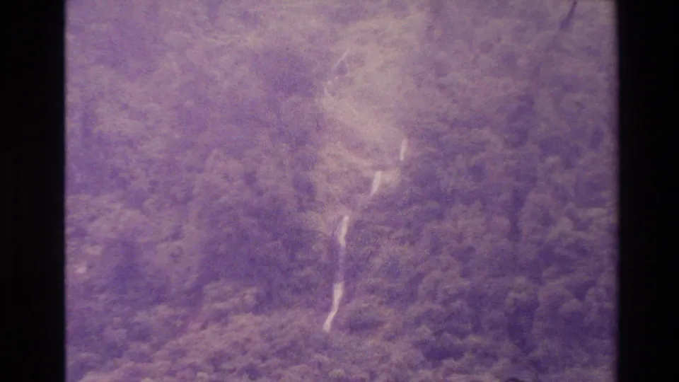 1982 New Zealand 8mm frame showing a brighter cascading waterfall descending through dense mountain vegetation.