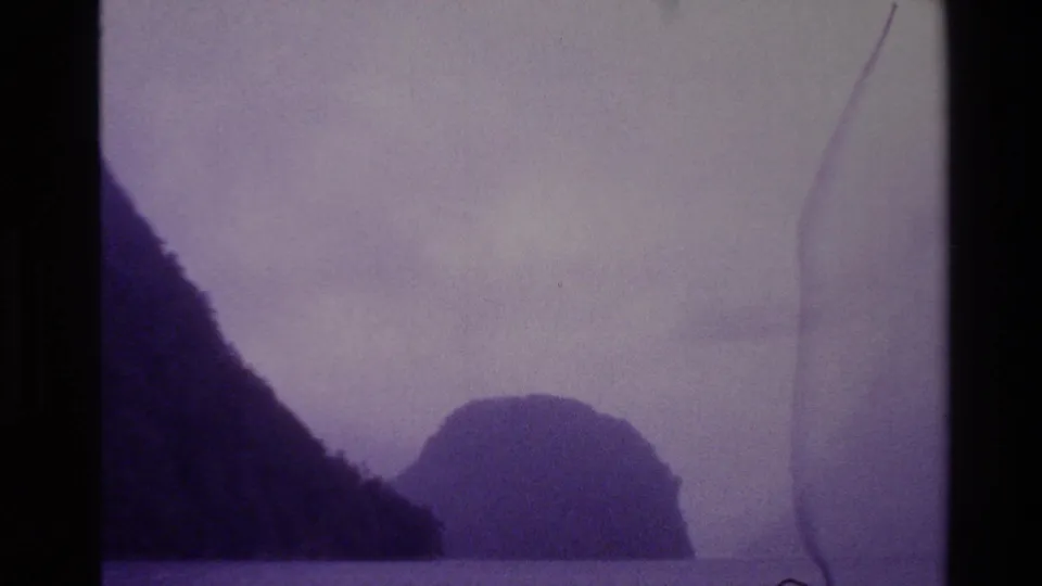 1982 New Zealand 8mm frame showing foggy water and rugged island silhouettes with visible film edge marks and faded color.