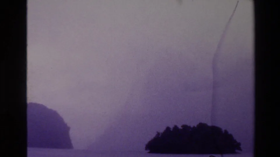 Purple-faded 8mm frame of misty New Zealand water with dark island forms at the lower edges and soft, low-contrast sky.