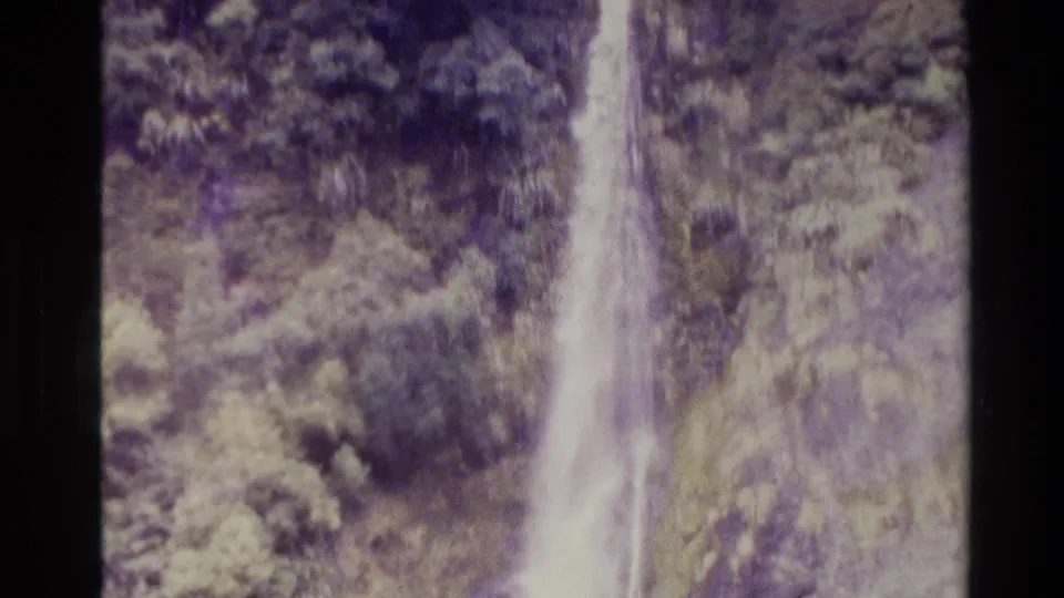 1982 New Zealand 8mm frame with a vertical waterfall passing over a rocky, tree-covered cliff in soft faded color.