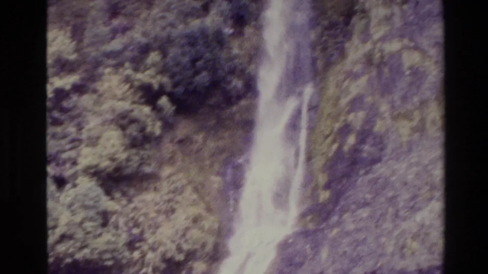 1982 New Zealand 8mm frame showing the lower section of a waterfall spilling down rock into a dark pool surrounded by vegetation.