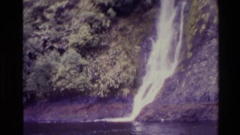 1982 New Zealand 8mm frame showing the waterfall’s lower drop and pool, with dense trees and rock softened by home-movie grain.