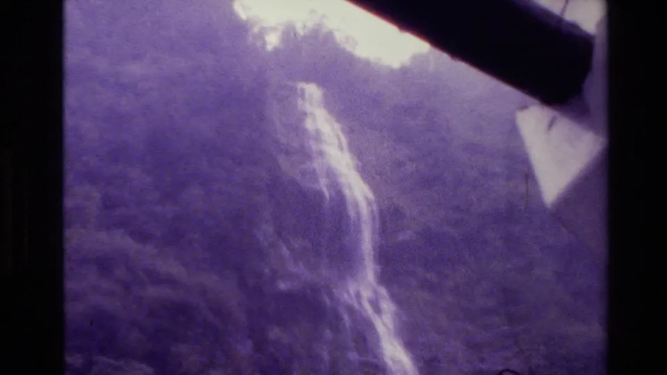New Zealand 1982 8mm frame showing a distant waterfall dropping down a wooded mountain slope.