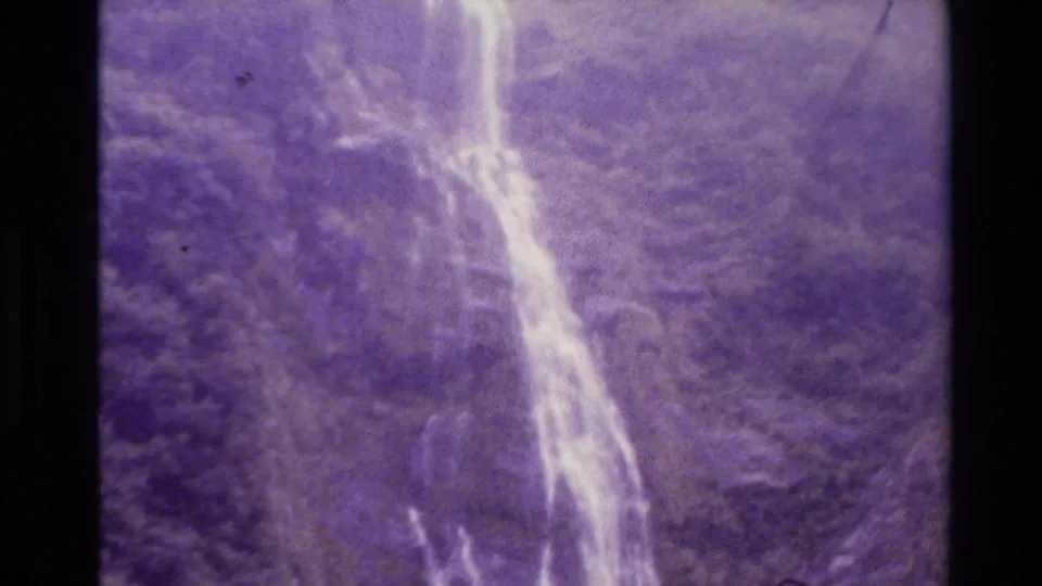 New Zealand 1982 home-movie frame of a waterfall cascading over rocks through dense mountain vegetation.