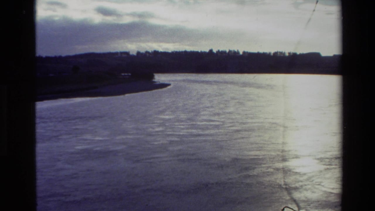1982 New Zealand 8mm frame showing a broad waterway with shoreline and cloudy sky, bordered by dark film edges.