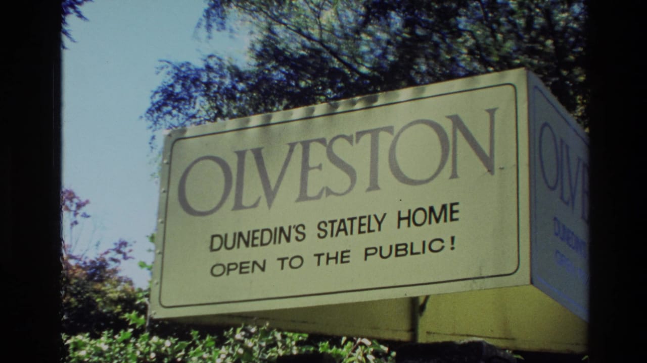 Olveston sign reading Dunedin's stately home open to the public, with trees behind it.