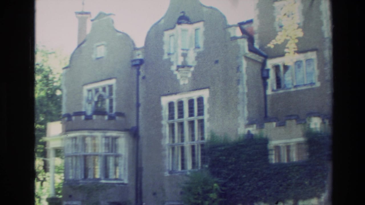 1982 New Zealand 8mm frame showing a large Tudor-influenced mansion facade with shaped gables, bay windows, and surrounding trees.