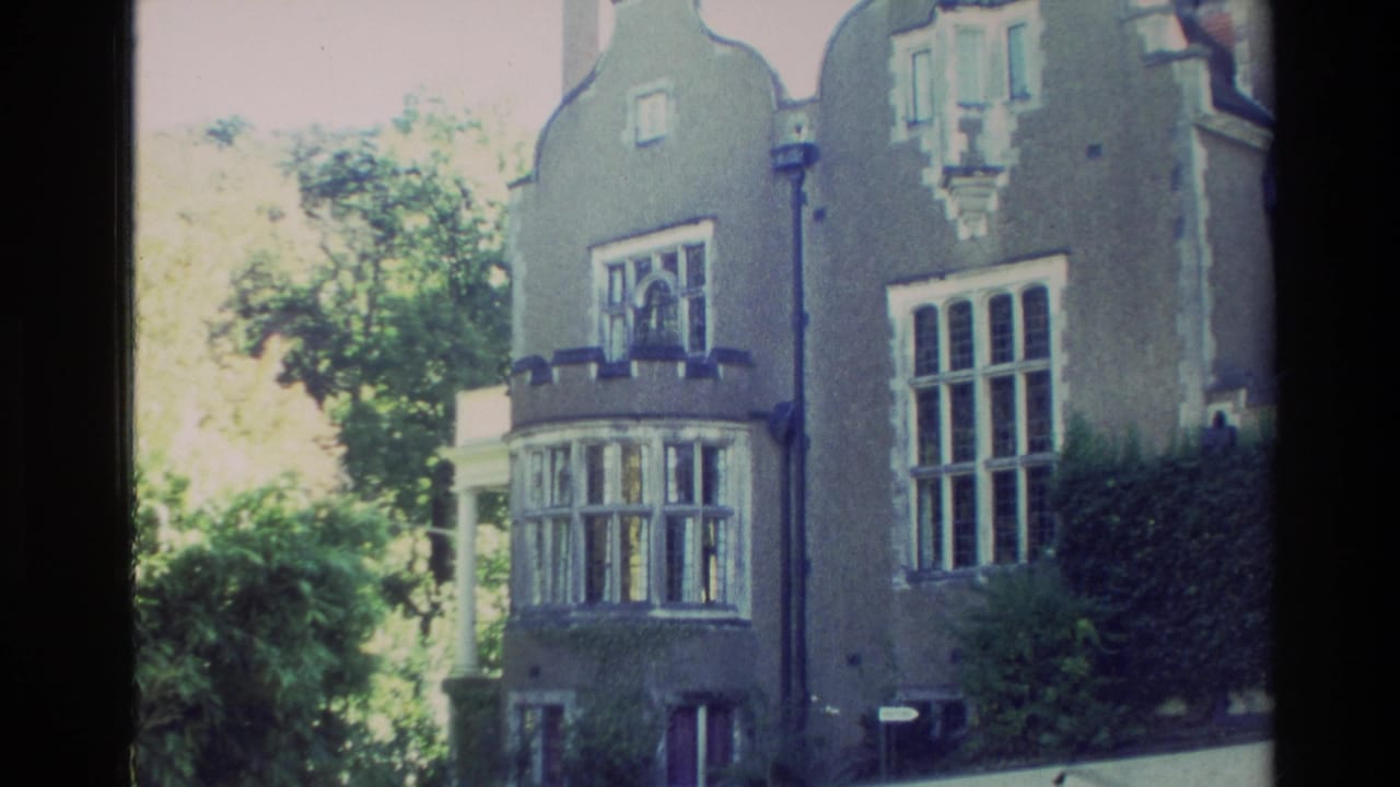 Closer view of the mansion facade with bay window, gables, trees, and hedge.